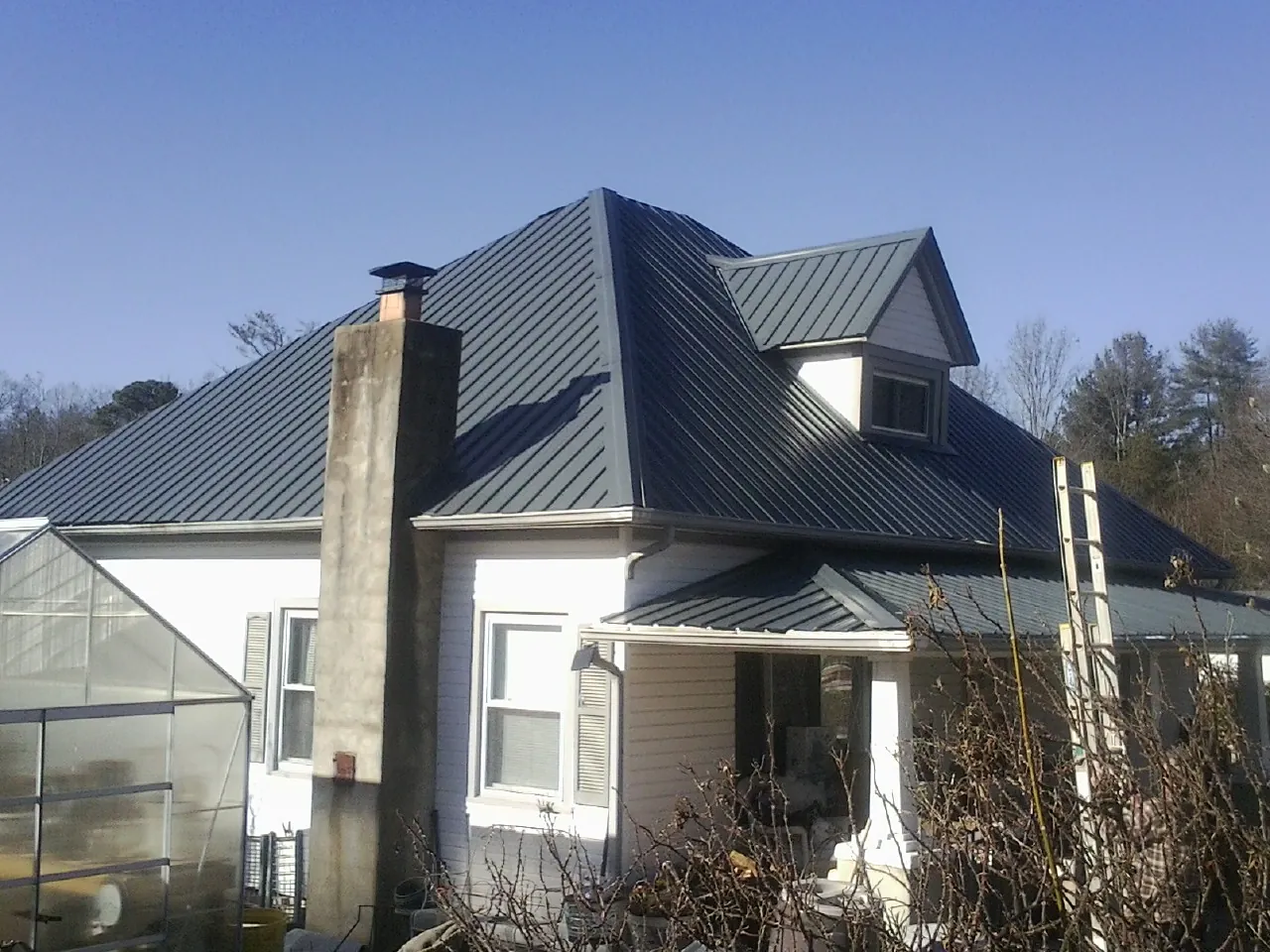 Dark blue standing seam metal roof on a white farmhouse with dormer — Slate & Tile Roof Repair by Roofing Brothers in Woodhull