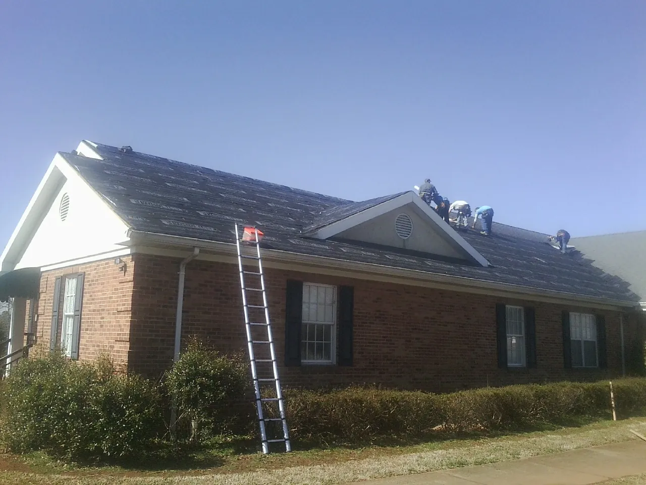 Crew tearing shingles off a brick ranch roof with a ladder set — Metal Roof Repair work by our crew in Woodhull