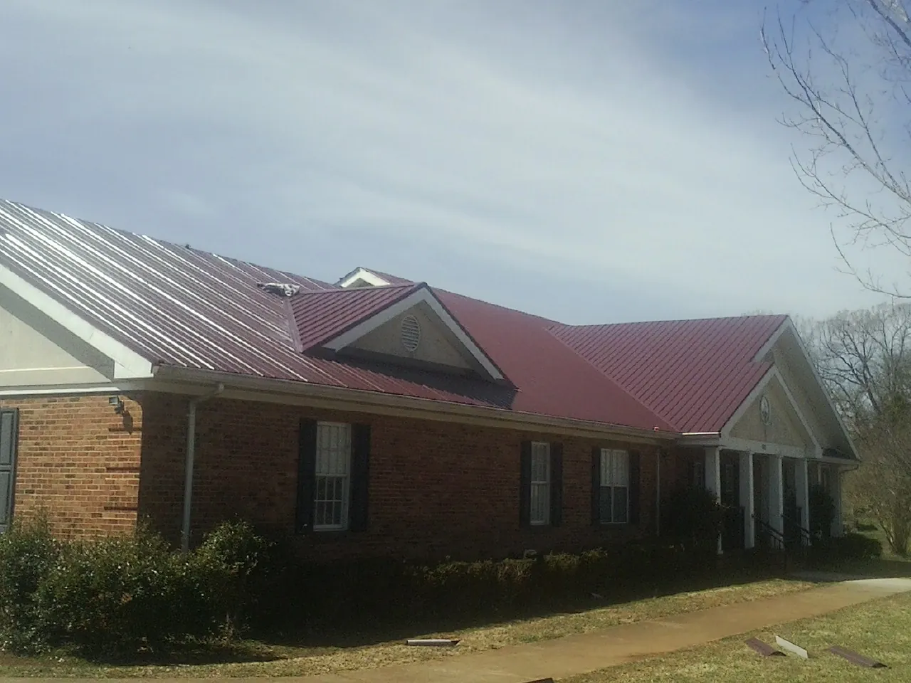 Red metal roof with gabled entries on a long brick building, from a Hail Damage Roof Repair job in Woodhull