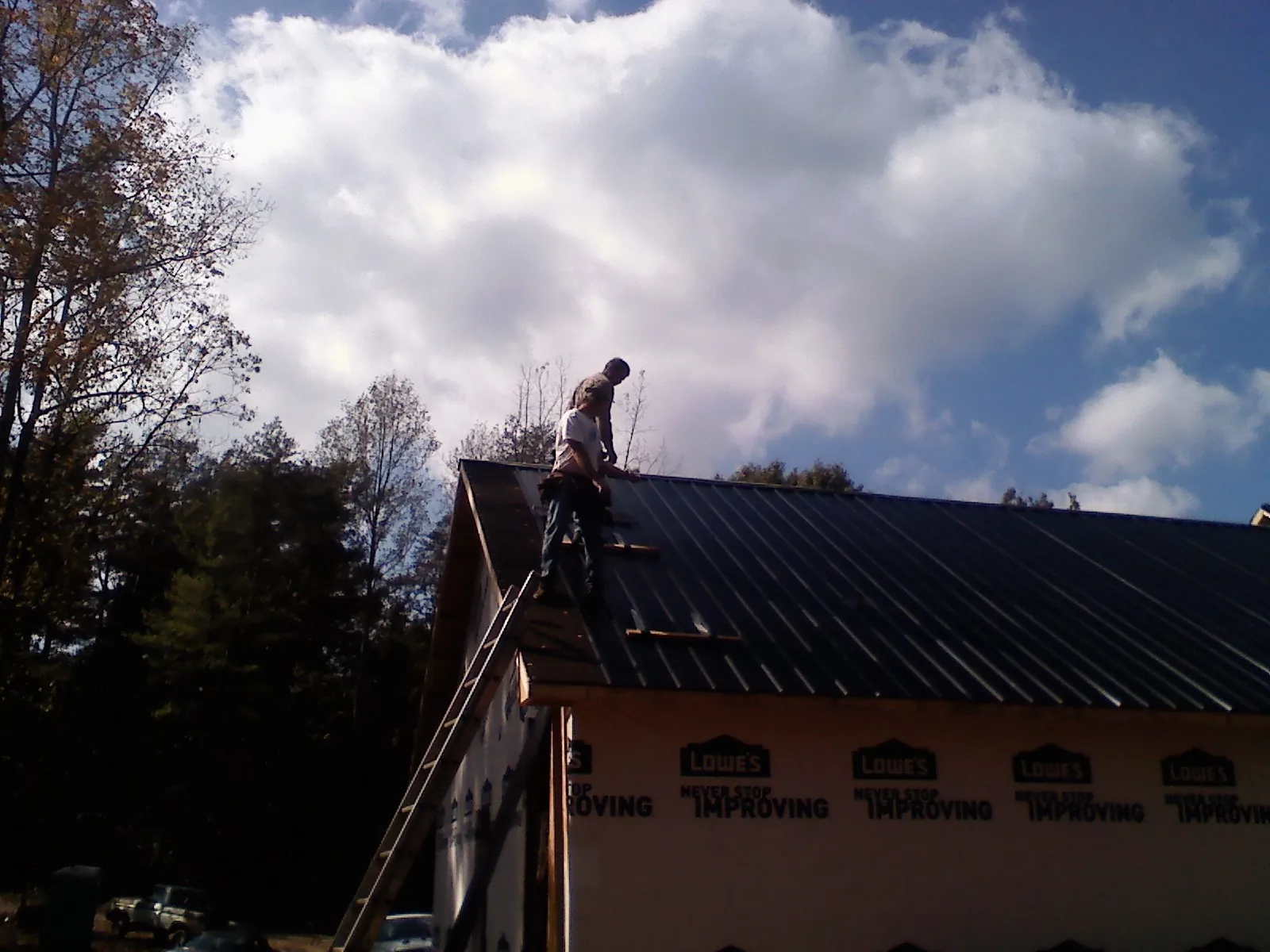 Roofer fastening dark metal panels high against a cloudy sky, from a Roof Inspection job in Woodhull