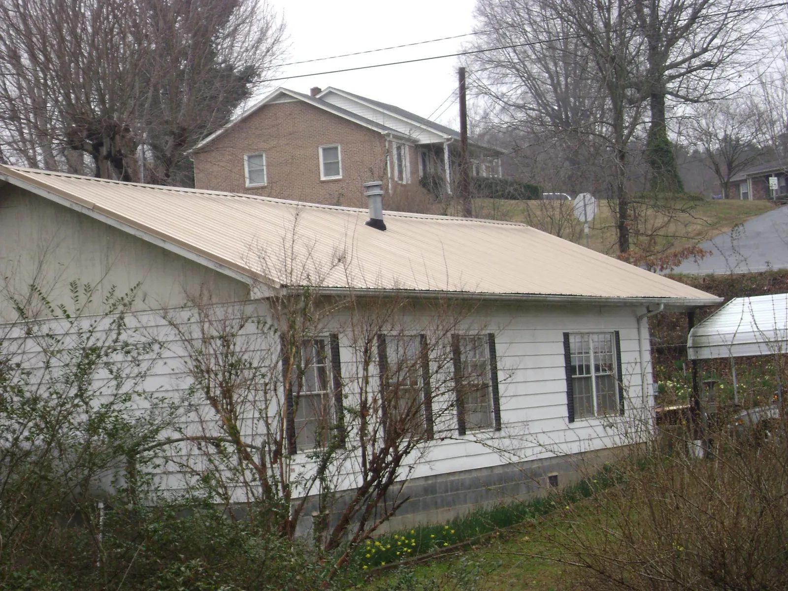 Tan metal roof on a white sided house set into a hillside — Commercial Roofing by Roofing Brothers in Woodhull